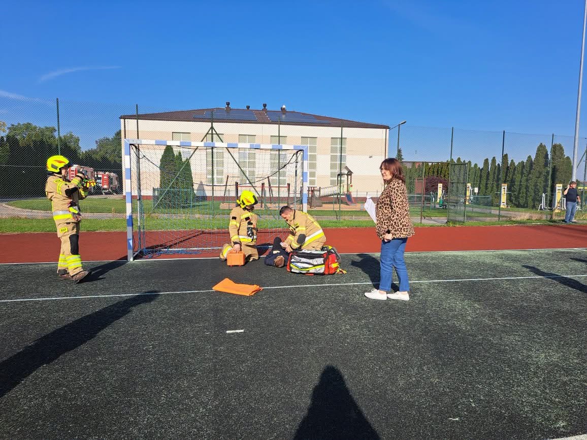 Strażacy podczas ćwiczeń przy bramce na szkolnym boisku.