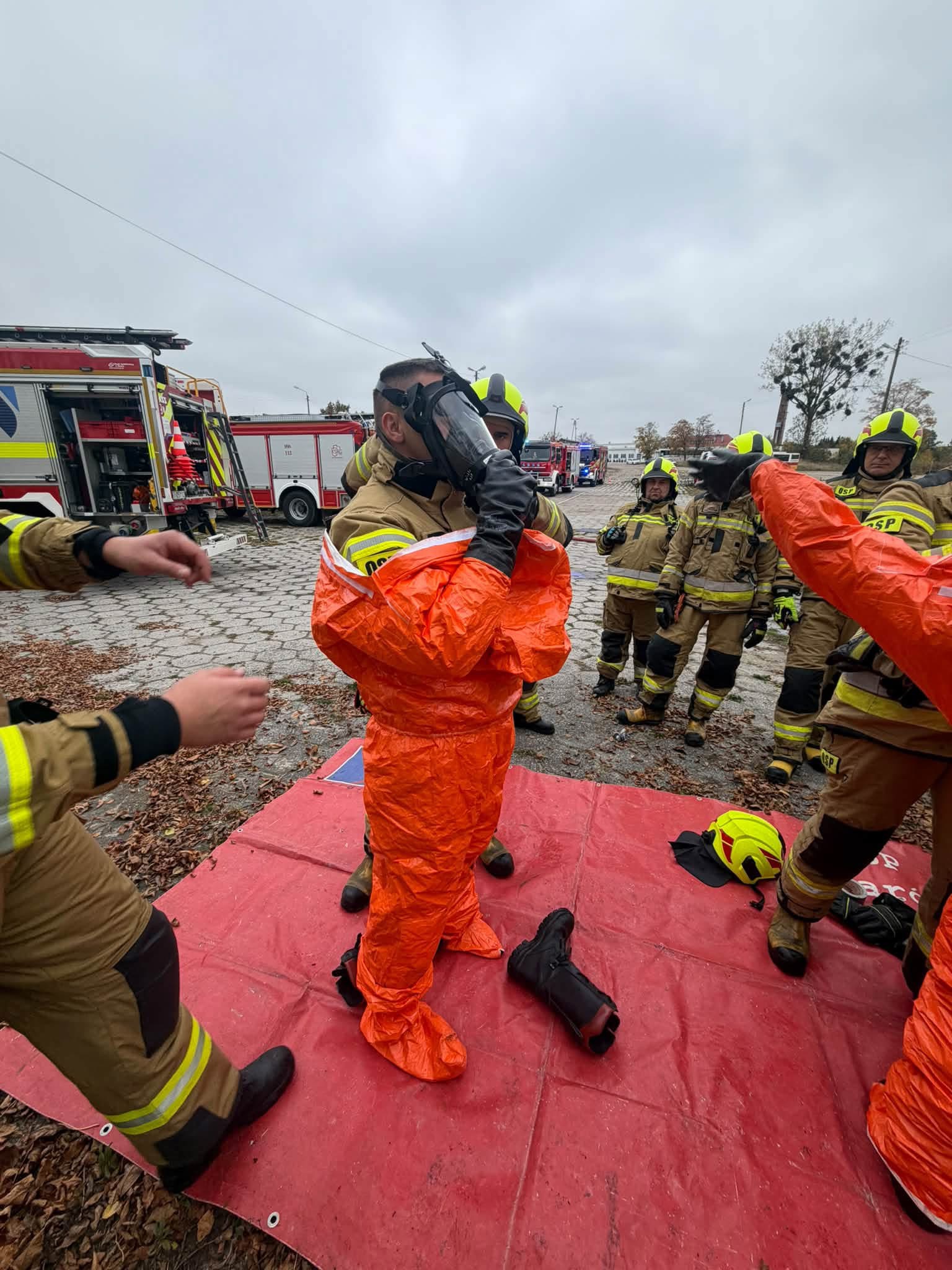Strażak zakłada pomarańczowy kombinezon ochronny podczas manewrów.