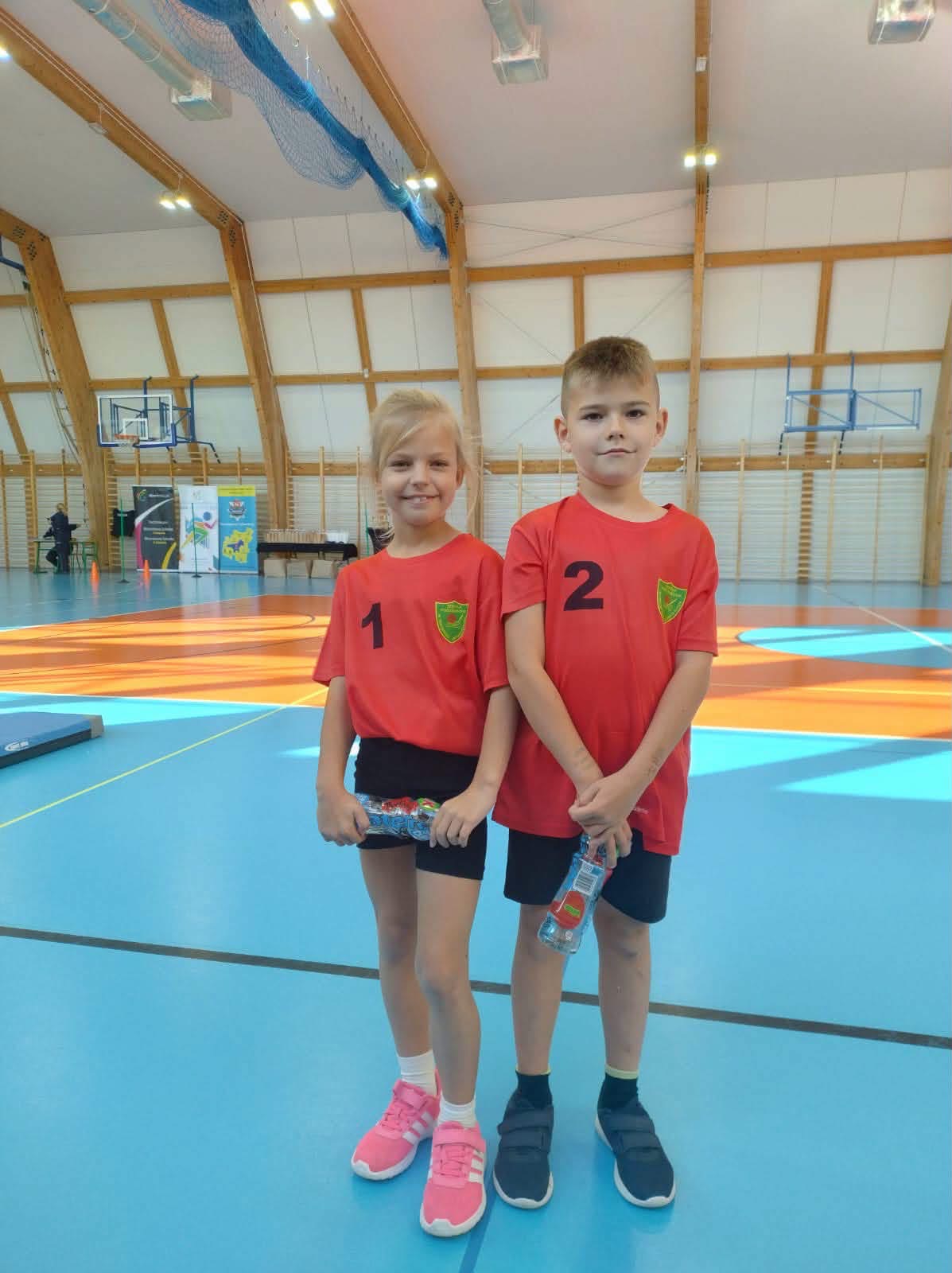 Dwoje uczniów w czerwonych koszulkach na hali sportowej.