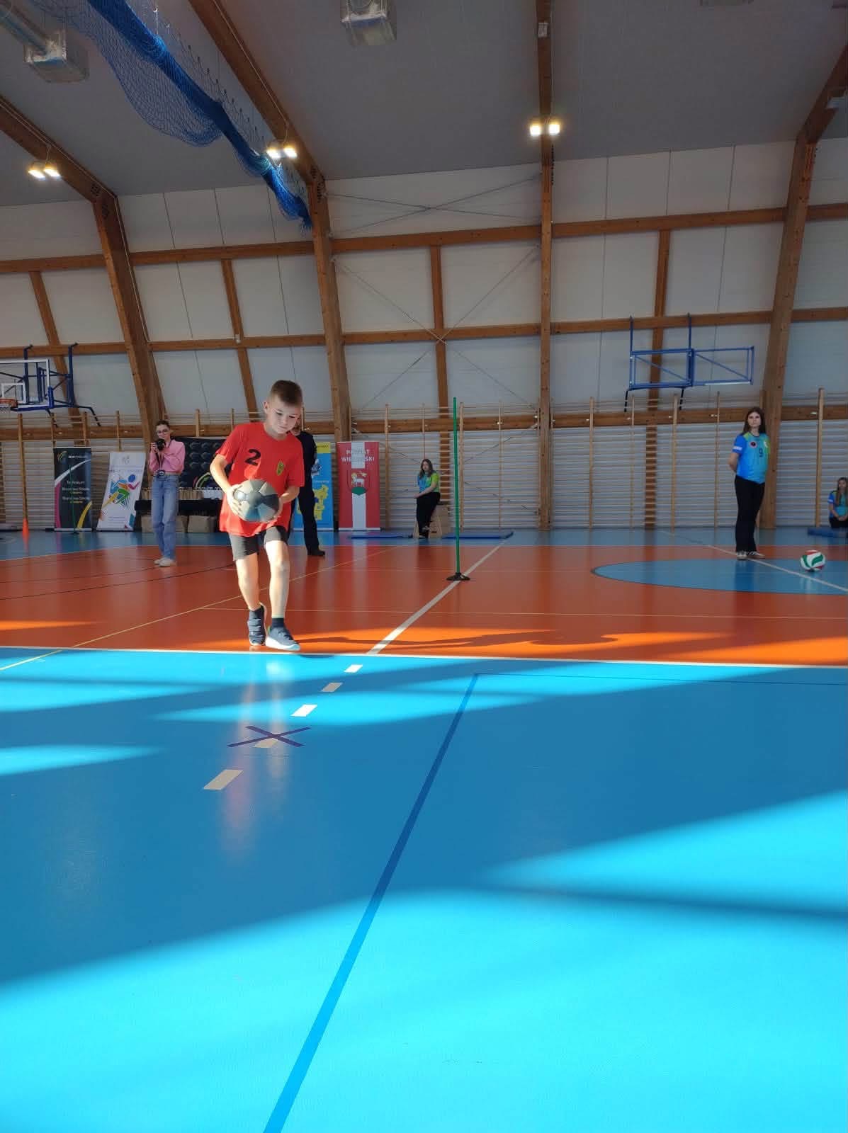 Uczeń szkoły w Rudzie podczas konkurencji z piłką na hali sportowej.