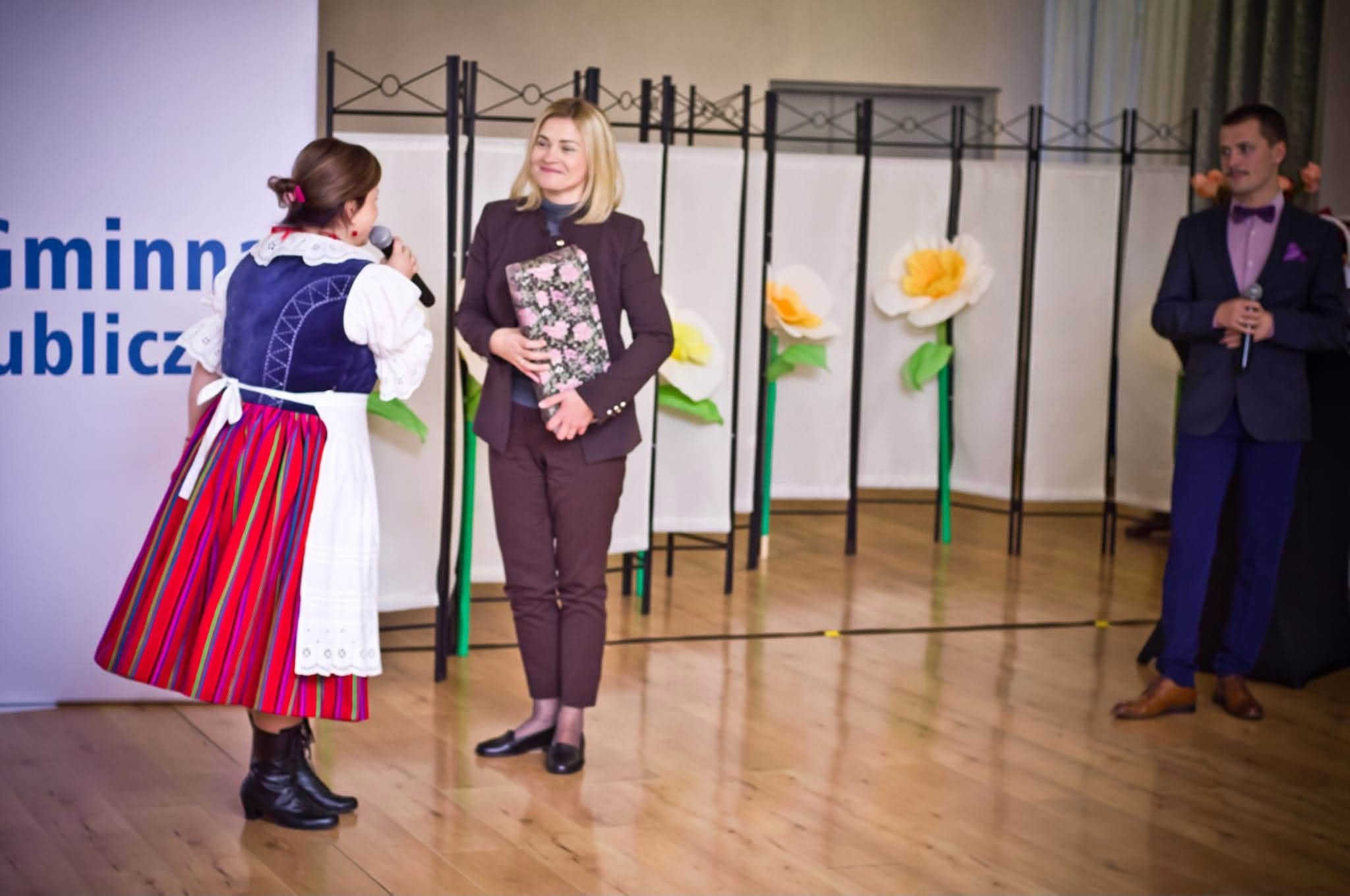 Przedstawicielka uroczystości rozmawia z zaproszoną uczestniczką trzymającą kwiaty.